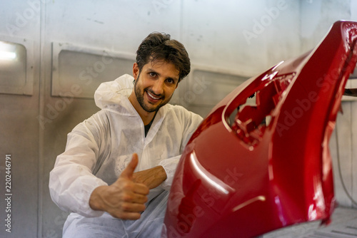 Smiling Mechanic Giving Thumbs Up Beside Red Car Bumper