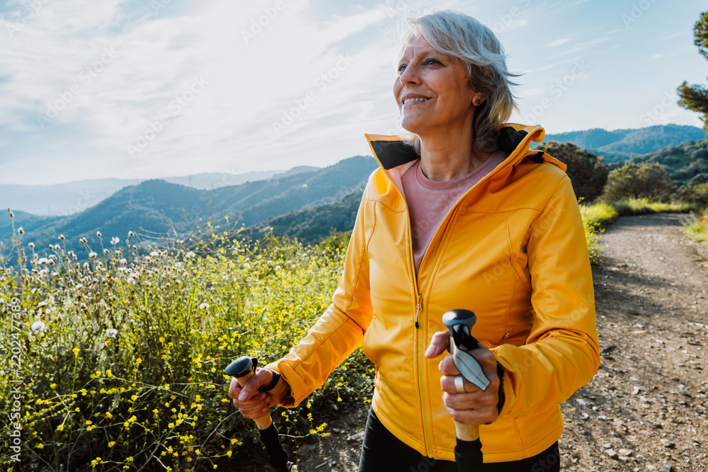 Fototapeta premium Active senior woman hiking on outdoor trail using trekking poles