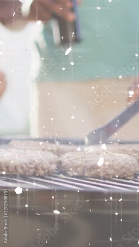Vertical video: Hand flipping burgers with tongs on grill cooking evenly, pal spraying oil, sparkle