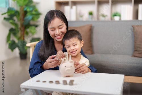 Asian mother teaching little son savings with piggy bank at home for financial literacy