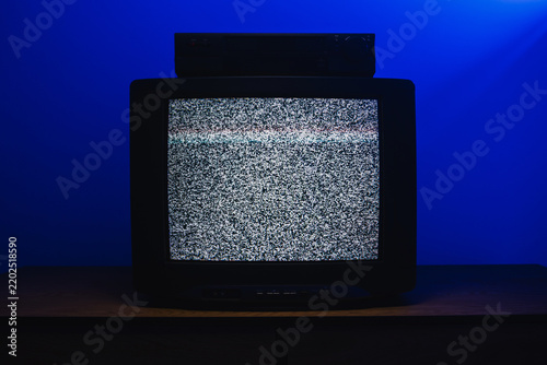 Retro CRT television with VCR displaying analog static interference in dark room with blue lighting