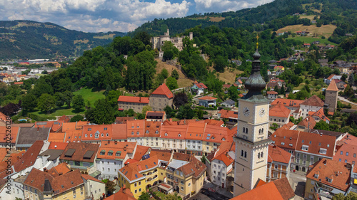 Aerial view of Wolfsberg town in Lavanttal valley, Carinthia. Historic city center with residential houses, streets, castle, and surrounding mountain hills on bright summer day.