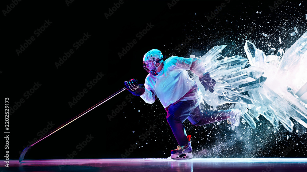 Obraz premium Hockey player skates through exploding ice crystals in dark studio with fierce competitive intensity. Winter sports, hockey advertising and athletic power concept.