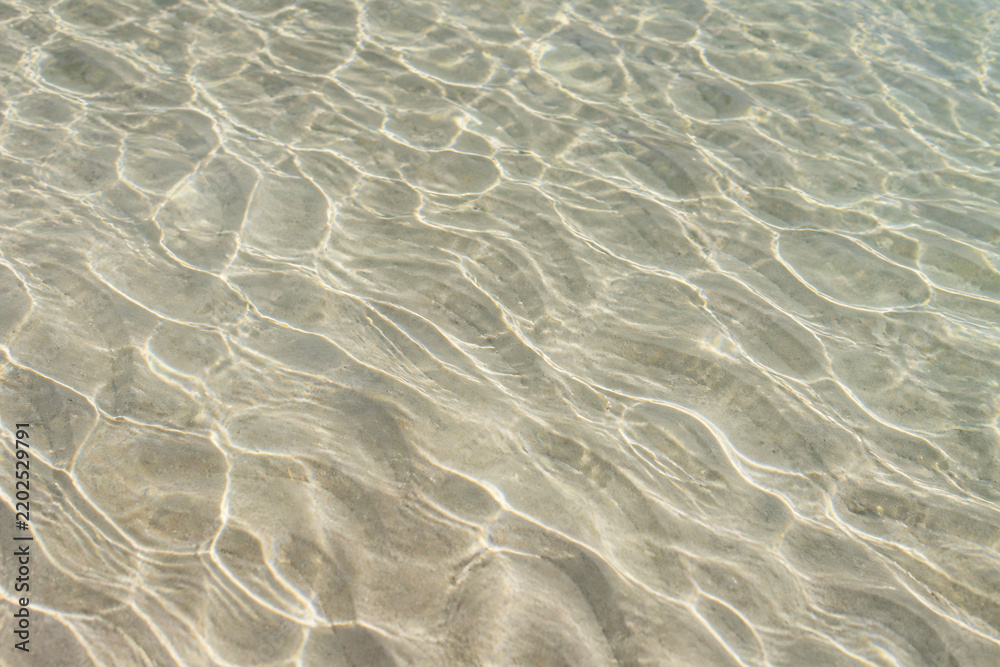 Fototapeta premium Sunlight filtering through clear water onto a sandy seabed, creating rippling patterns.