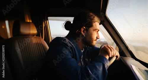 Contemplative man sits behind the wheel watching the coast at sunset