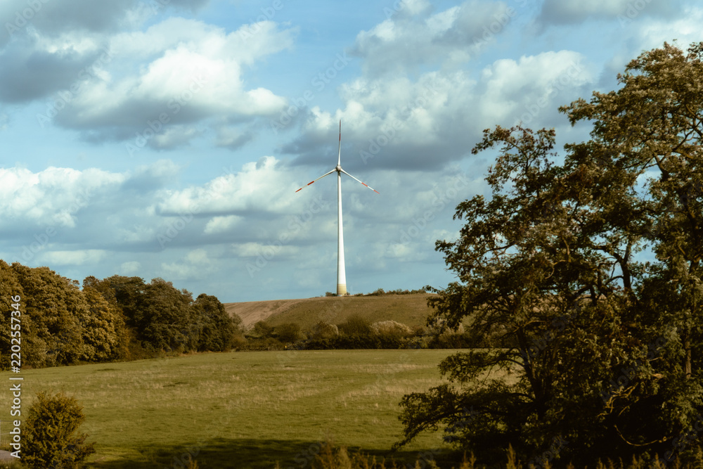 Obraz premium Wind turbine in green agricultural landscape under dramatic cloudy sky
