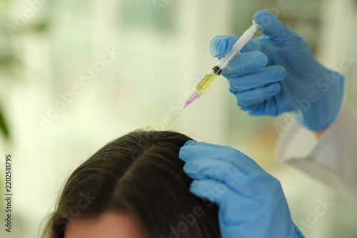 Photography Blue gloved hands hold syringe over parted scalp of dark-haired patient, deliver