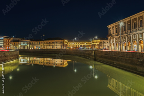 View of the illuminated historic buildings and Portici Ercolani reflected in the Misa River at night in Senigallia, Marche, Italy.