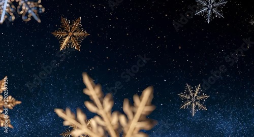Snowflakes made of gold and silver fall in a dark night sky during winter