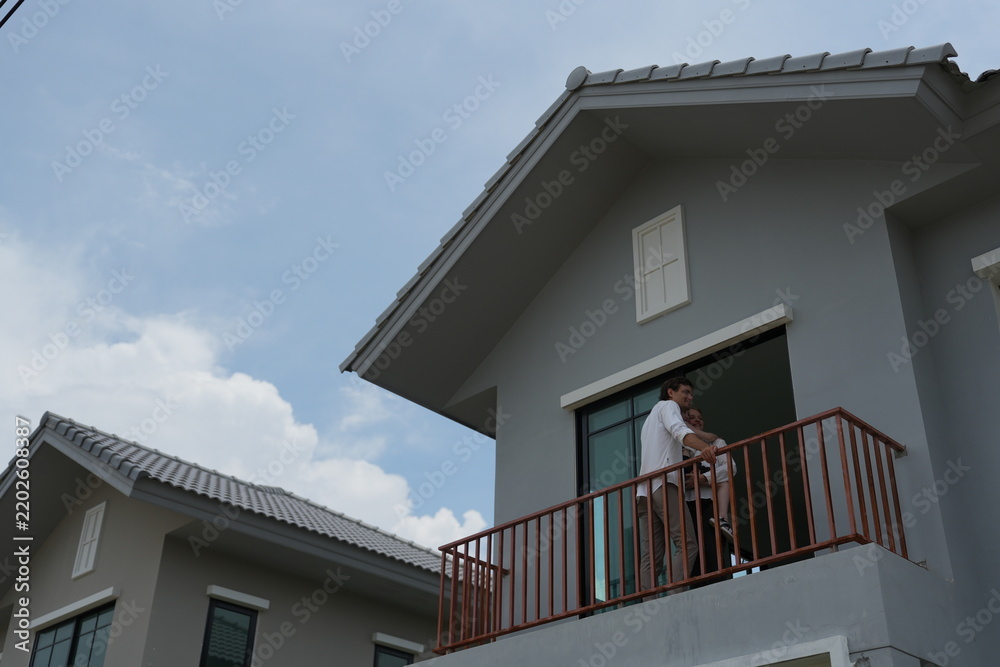 Obraz premium Caucasian family of three embracing stand at the wooden railing admiring the neighborhood view on the balcony of their new house overlooking the residential estate with copy space