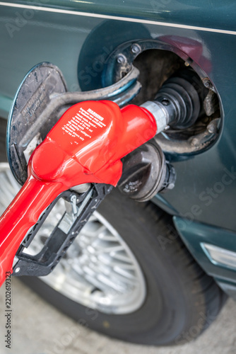 View of a red fuel nozzle inserted into a car's fuel tank filler neck at a gas station in Portland, Oregon, United States.