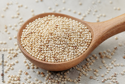 A wooden spoon filled with small, light-colored grains of quinoa rests on a light surface scattered with more quinoa.