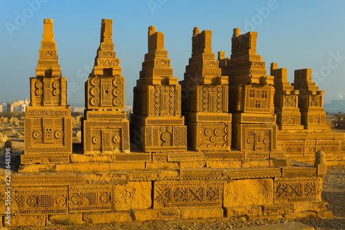 Karachi, Pakistan - 22 January 2010: View of the historic Chaukhandi Tombs featuring intricate sandstone carvings and pyramidal structures under a clear blue sky.