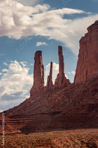 Oljato-Monument Valley, Arizona, United States - 05 September 2018: View of the Three Sisters rock formation, featuring towering red sandstone spires against a blue sky with clouds.