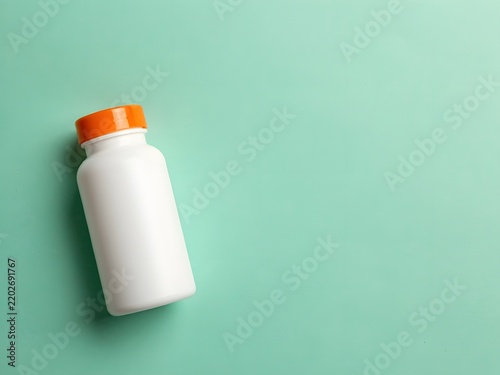 White plastic supplement bottle with orange cap on pastel green background