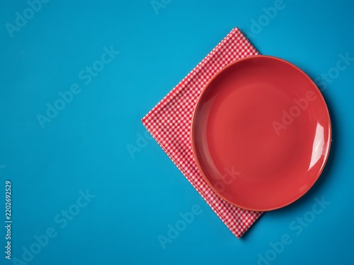 Top-down view of a red ceramic plate on a checkered napkin with copy space in a studio setting