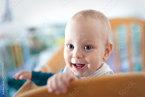 Fotografie A cheerful baby leans over the wooden crib, flashing a big smile