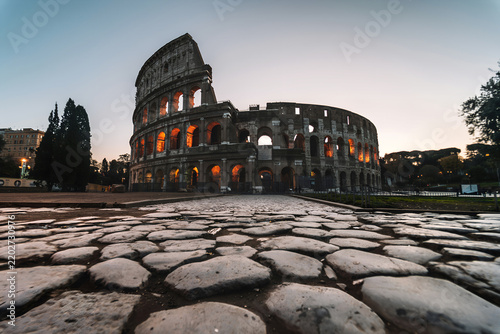 Colosseum in Rome, Italy at Dusk with Warm Interior Lights Ancient Roman Amphitheater Along Historic Cobblestone Road
