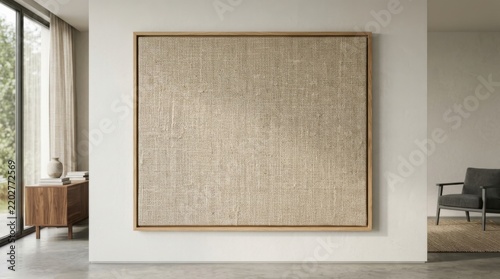 Large square canvas with textured beige fabric art in a minimalist wooden frame hanging on a clean white wall interior