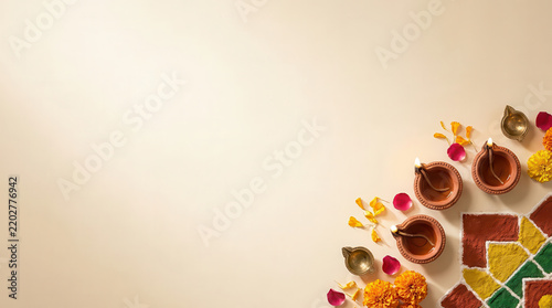 Elegant Diwali festive background with traditional diyas, colorful rangoli patterns, sweets and flower petals arranged along the lower right corner, with spacious cream copy space for greetings