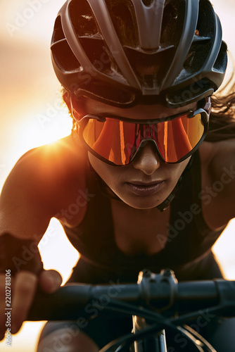 A close‑up of a female cyclist wearing a helmet and sports glasses, illuminated by the warm rays of the sun during her ride.