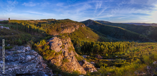 A sunlit rocky cliff overlooks a sweeping landscape
