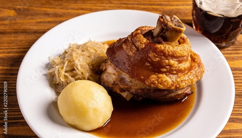 Crispy roasted pork knuckle served with potato dumpling, sauerkraut, and savory dark beer gravy on a plate, traditional Bavarian cuisine in a rustic restaurant