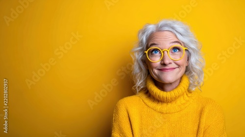 A cheerful senior woman smiles while wearing a bright yellow sweater, exuding happiness and warmth against a vivid yellow background, embodying joy and positivity.