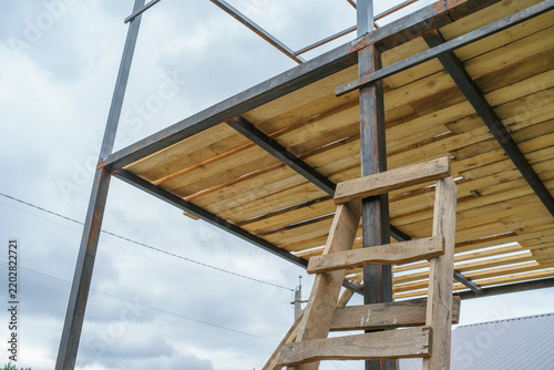 Fotografía A tubular metal framework of a building under construction, featuring a wooden plank floor and a staircase to the second level