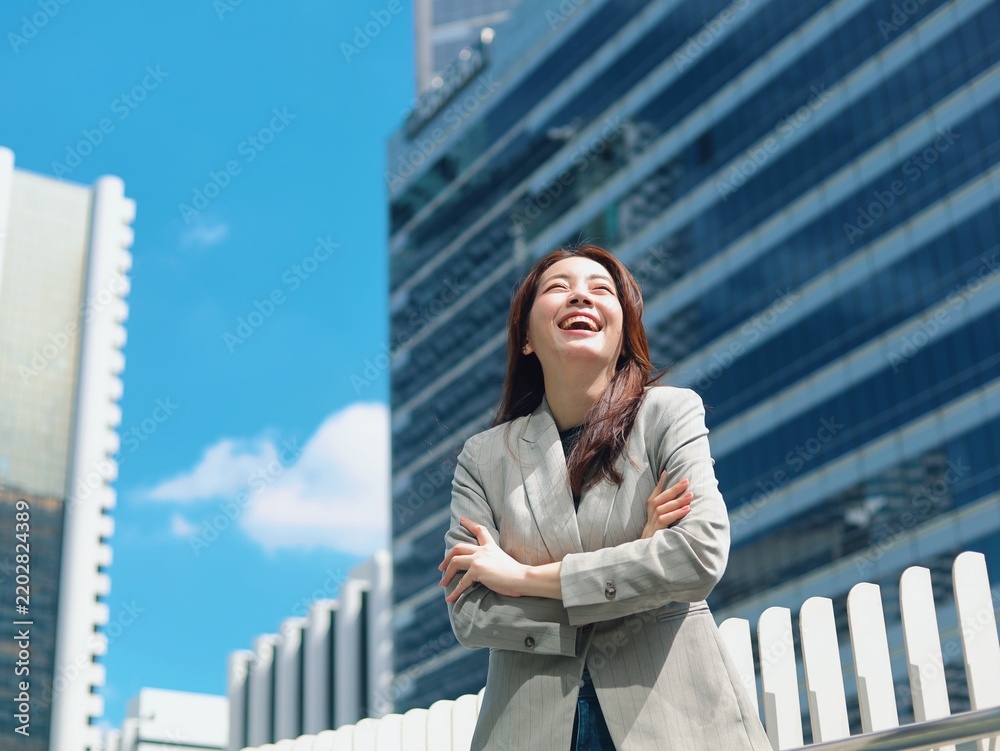 Fototapeta premium Confident young Asian businesswoman smiling outdoors in a modern urban environment with office buildings in the background.