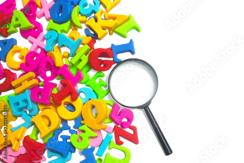 Bright, colorful magnetic alphabet letters scattered on a white background beside a magnifying glass.