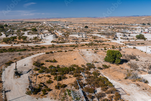 Aerial perspective of numerous pump jacks and industrial pipelines distributed across an arid oil field landscape under clear skies, illustrating petroleum extraction and energy infrastructure.