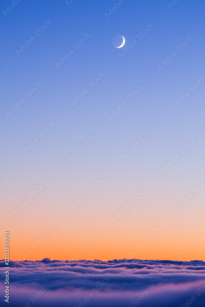 Fototapeta premium Crescent moon shining in a vibrant twilight sky above a thick layer of soft rolling clouds