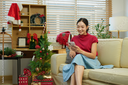 Young woman using smartphone at home during Christmas holiday. Asian female texting on mobile phone banner. Communication, connection, online shopping, winter lifestyle concept