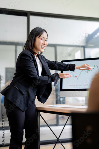 Young Asian businesswoman presenting financial market data and stock analysis on a computer monitor during a business meeting in office