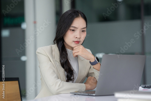Young businesswoman with a serious expression concentrating on a laptop screen, thinking about business strategy or problem solving
