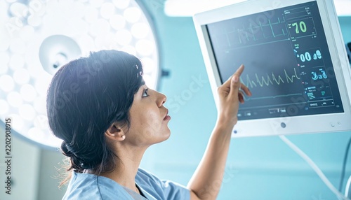 Nurse examines patient monitor displaying vital signs in operating room