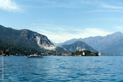Scenic view of a passenger boat cruising on a blue lake with mountains and traditional Italian style island in the background