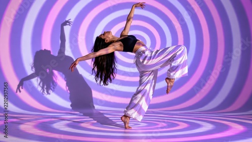 Woman dancing with arms raised against a purple and pink concentric circle background with woman long