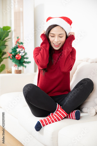 Foto Cheerful Woman in Santa Hat Sitting on Sofa at Home During Christmas
