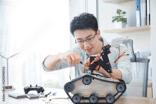 Young engineer assembling a tracked robot in a bright office workspace