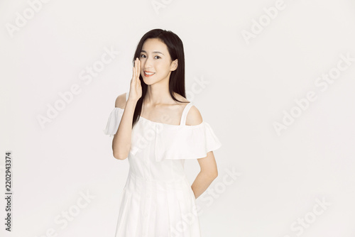 Smiling young woman in a white dress gesturing against a white background