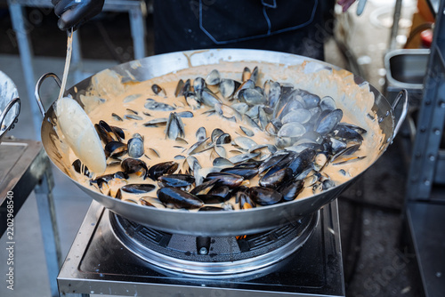 Картината върху платно Pan of mussels simmering in creamy sauce with ladle