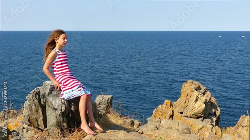 Little girl sitting on rocky shore of sea