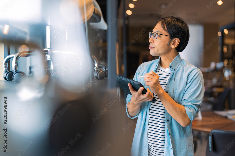 Obraz premium Focused Asian store supervisor using digital tablet to inspect showroom stock, auditing product quality and retail inventory management with professional diligence in modern furniture design store