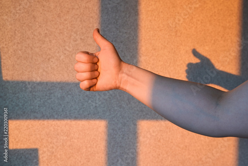 Obraz na płótnie Raised Thumb And Forearm Casting Shadow Across Sunlit Textured Wall Beside Window Grid In Warm Late Afternoon Interior Light