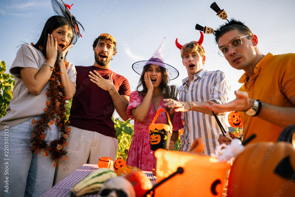 Obraz premium Group of surprised friends in Halloween costumes making shocked expressions towards the camera at an outdoor party.