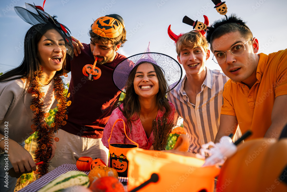 Obraz premium Close-up of laughing young friends wearing Halloween headbands and costumes gathered together outdoors.