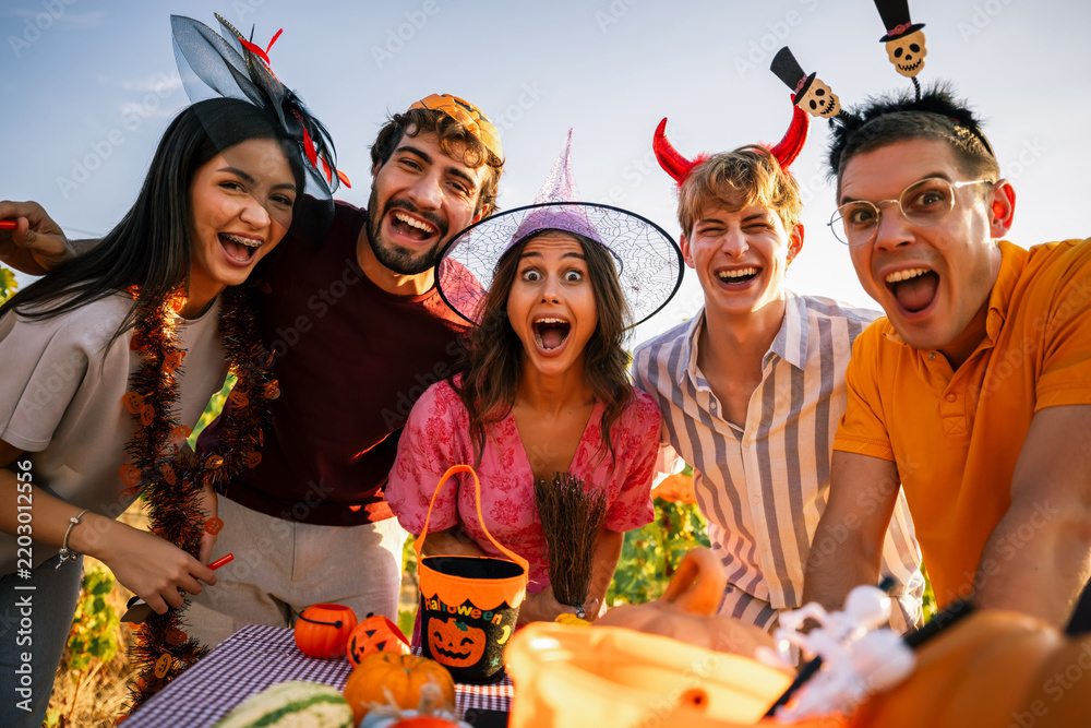 Obraz premium Group of excited young friends wearing Halloween costumes shouting and cheering at an outdoor autumn event.