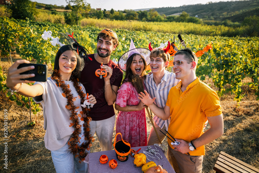 Obraz premium Young woman taking a group selfie with friends in Halloween costumes in a sunny vineyard.